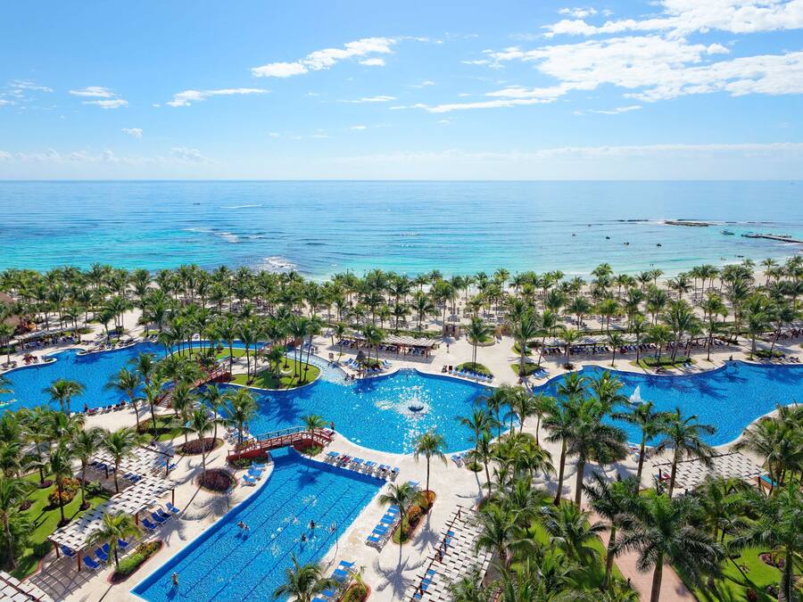 Een resort met verschillende zwembaden, palmbomen en uitzicht op de oceaan.