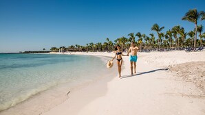Una playa con agua turquesa cristalina, palmeras y gente caminando por la orilla.
