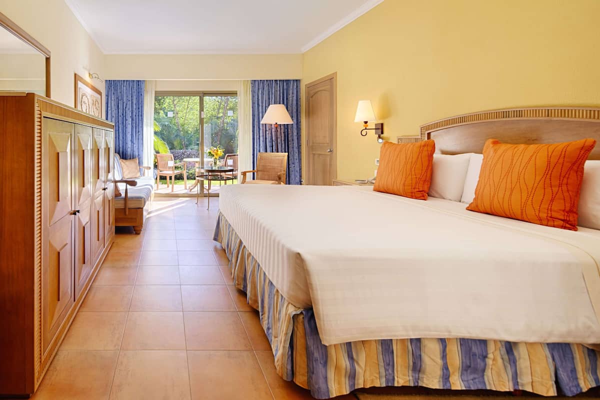 A hotel room with a large bed, a wooden wardrobe, a desk with a chair, and a balcony with a table and chairs.