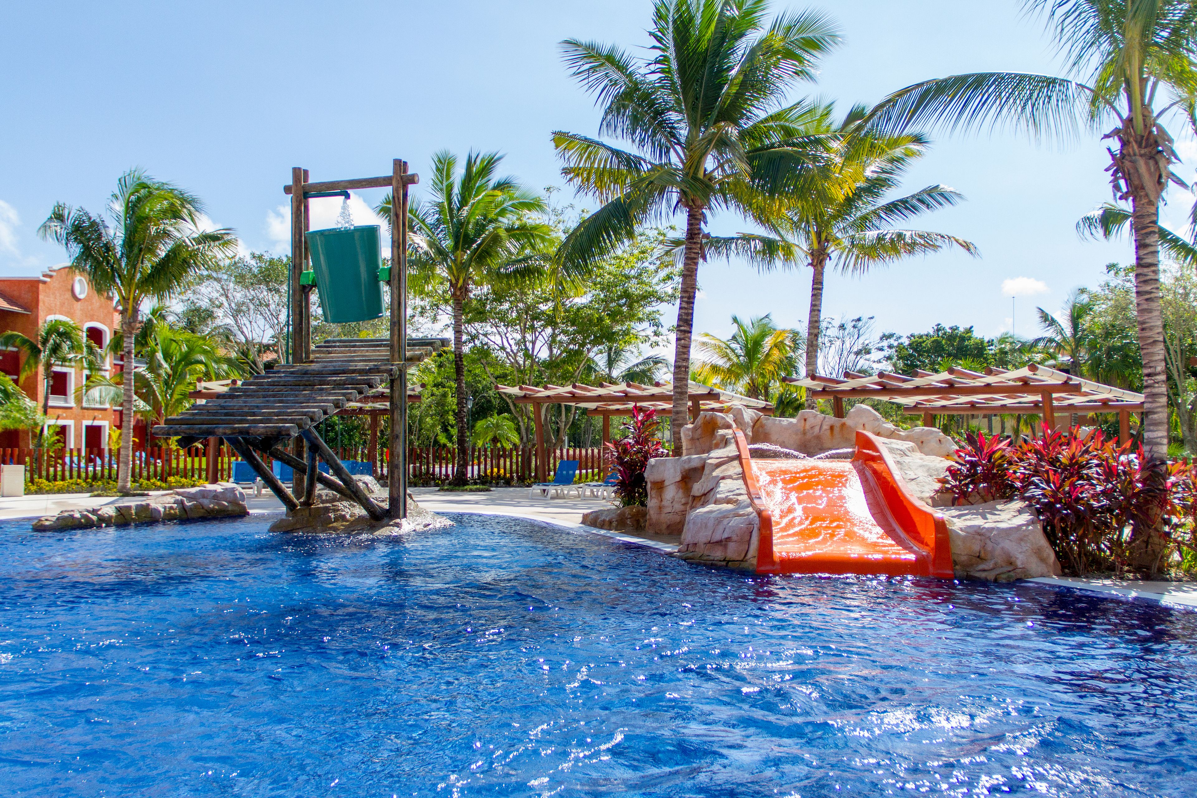 Una piscina con tobogán, palmeras y un edificio al fondo.