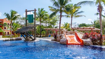 Una piscina con tobogán, palmeras y un edificio al fondo.