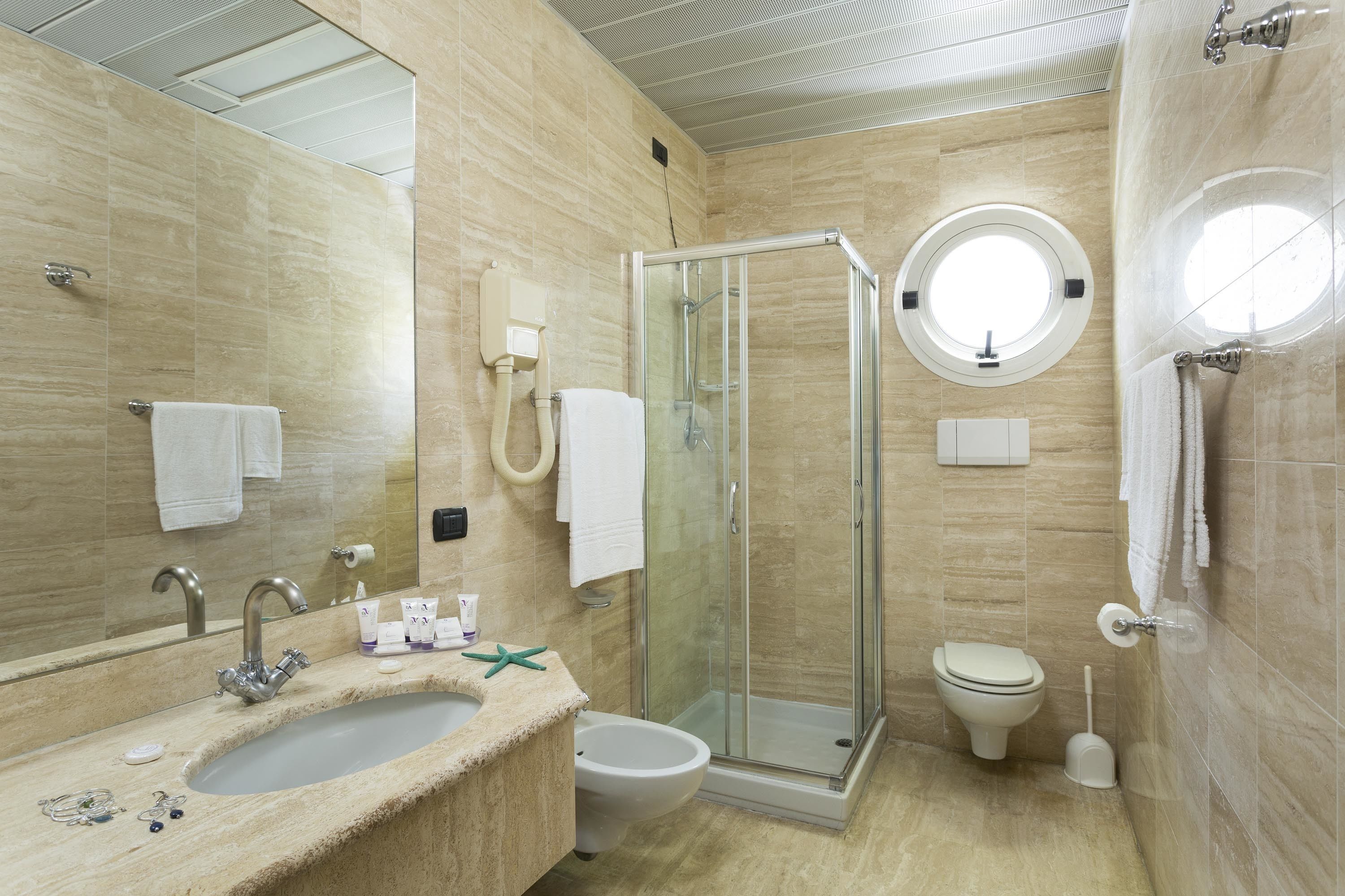 A modern bathroom with a glass-enclosed shower, a round mirror, a sink, and a toilet.