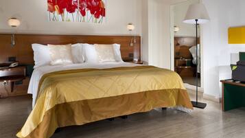 Una camera d'albergo con un letto grande, un comodino, una lampada e un quadro con fiori rossi al muro.