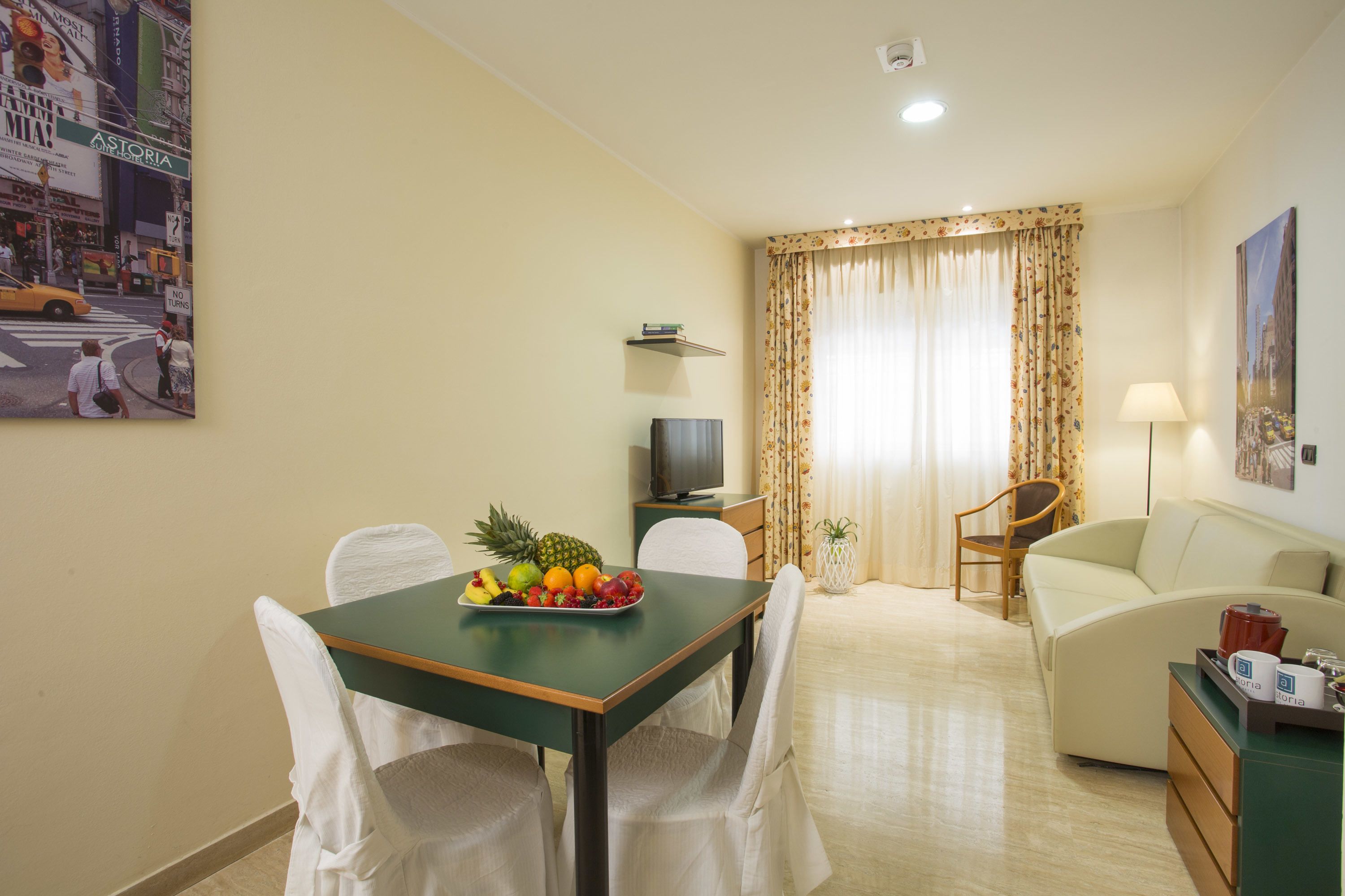 Habitación de hotel con comedor, sofá, televisor y frutero sobre la mesa.