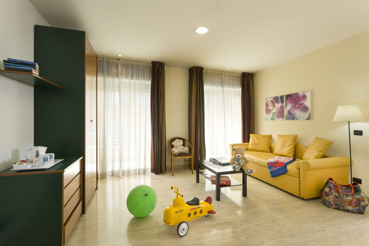 A living room with a yellow sofa, a green exercise ball, a toy car, and a teddy bear.