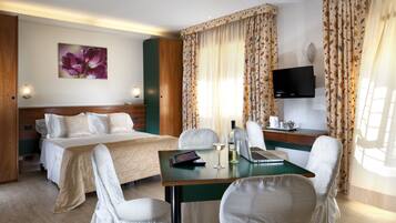 A hotel room with a bed, two chairs, a desk with a laptop, a TV, and a floral curtain.