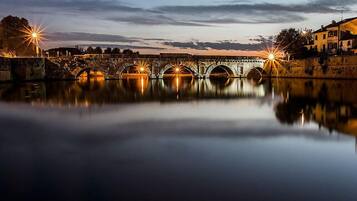 A historic stone bridge with multiple arches over a calm river, reflecting the lights from the surrounding buildings.