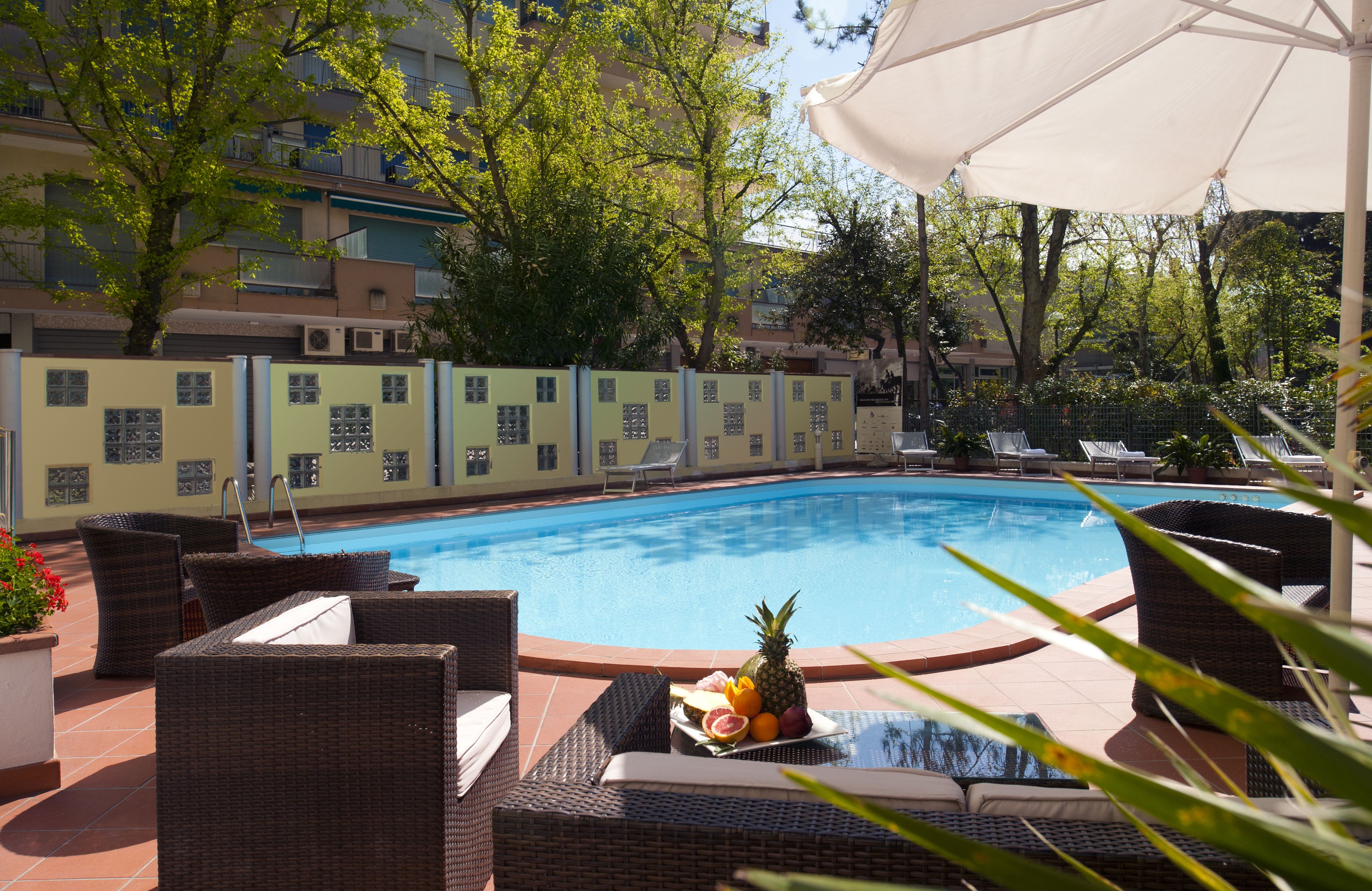 A poolside area with wicker lounge chairs, a fruit bowl, and a white umbrella.
