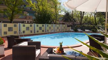 A poolside area with wicker lounge chairs, a fruit bowl, and a white umbrella.