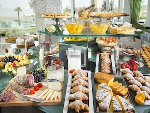 A buffet with various food items including pastries, fruits, cheeses, and meats.