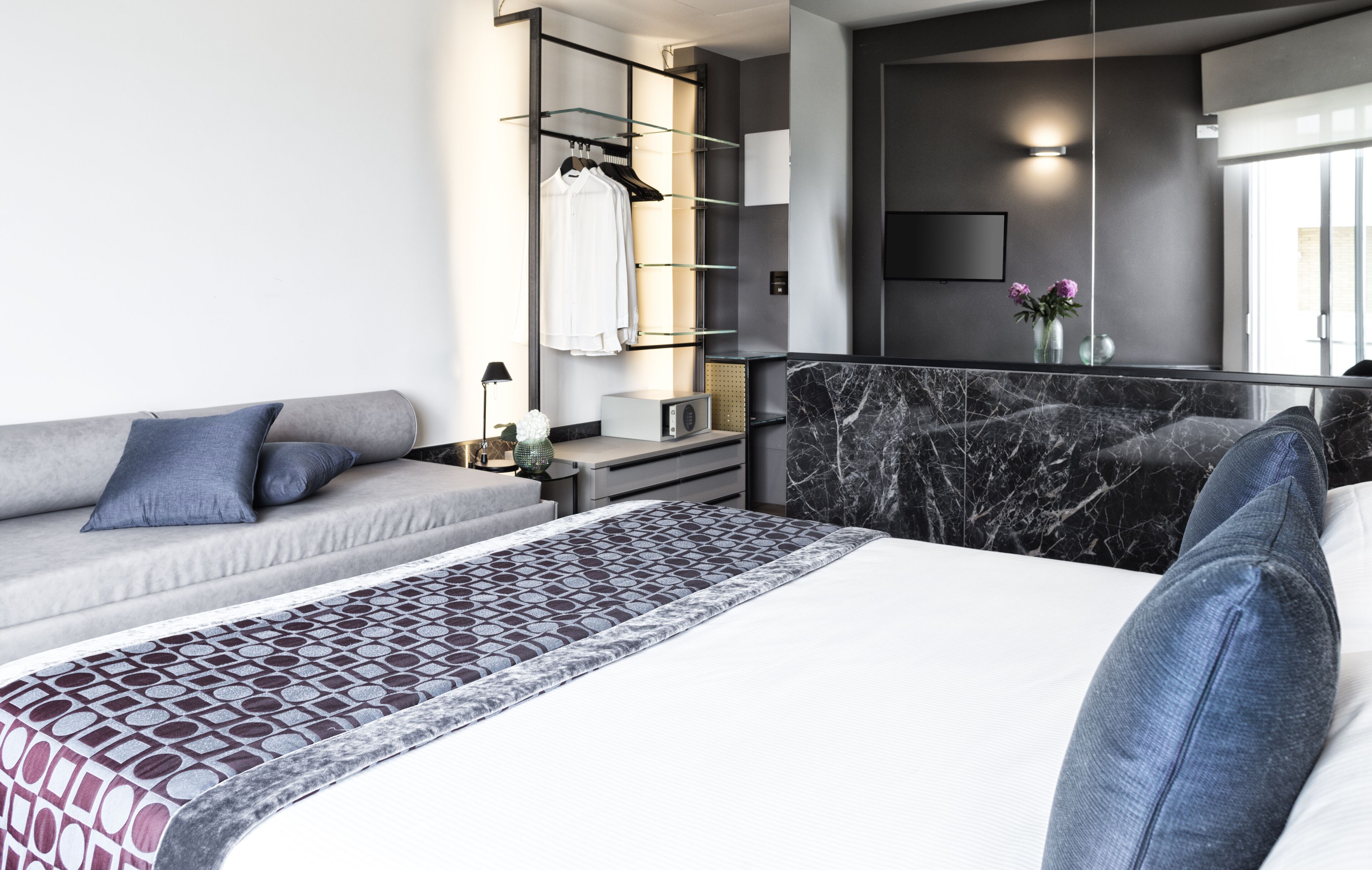 Ett modernt hotellrum med en säng, en soffa, en TV, en spegel och en garderob.