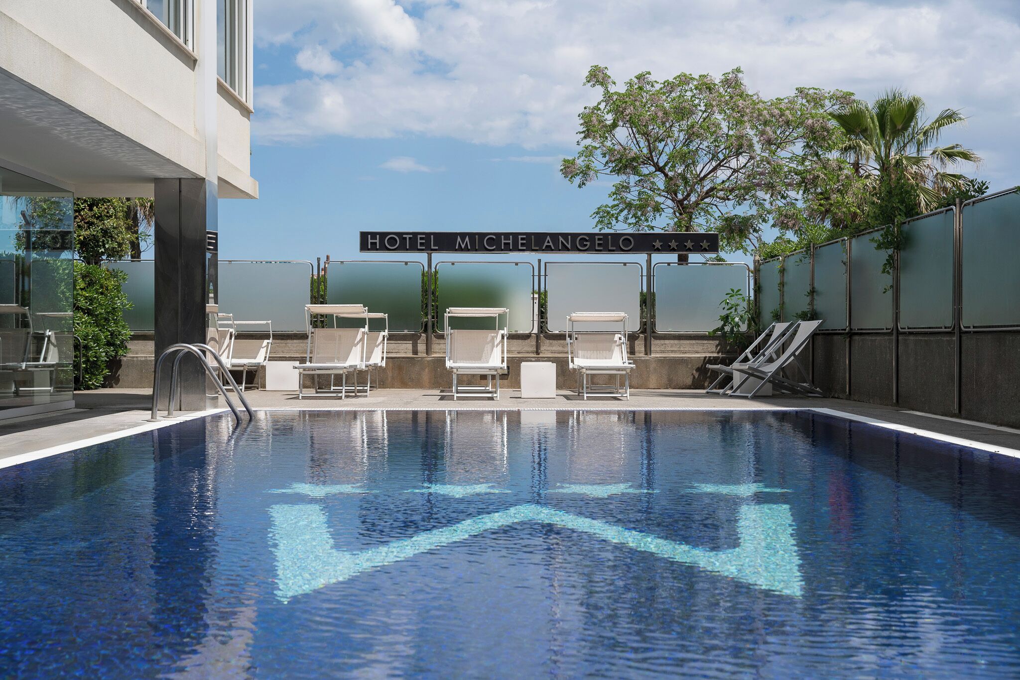 Una piscina con sillas de descanso y un cartel que indica Hotel Michelangelo.