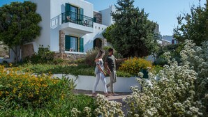 A modern house with a balcony, surrounded by lush greenery and flowering plants. - Naxos Palace Hotel (Naxos)