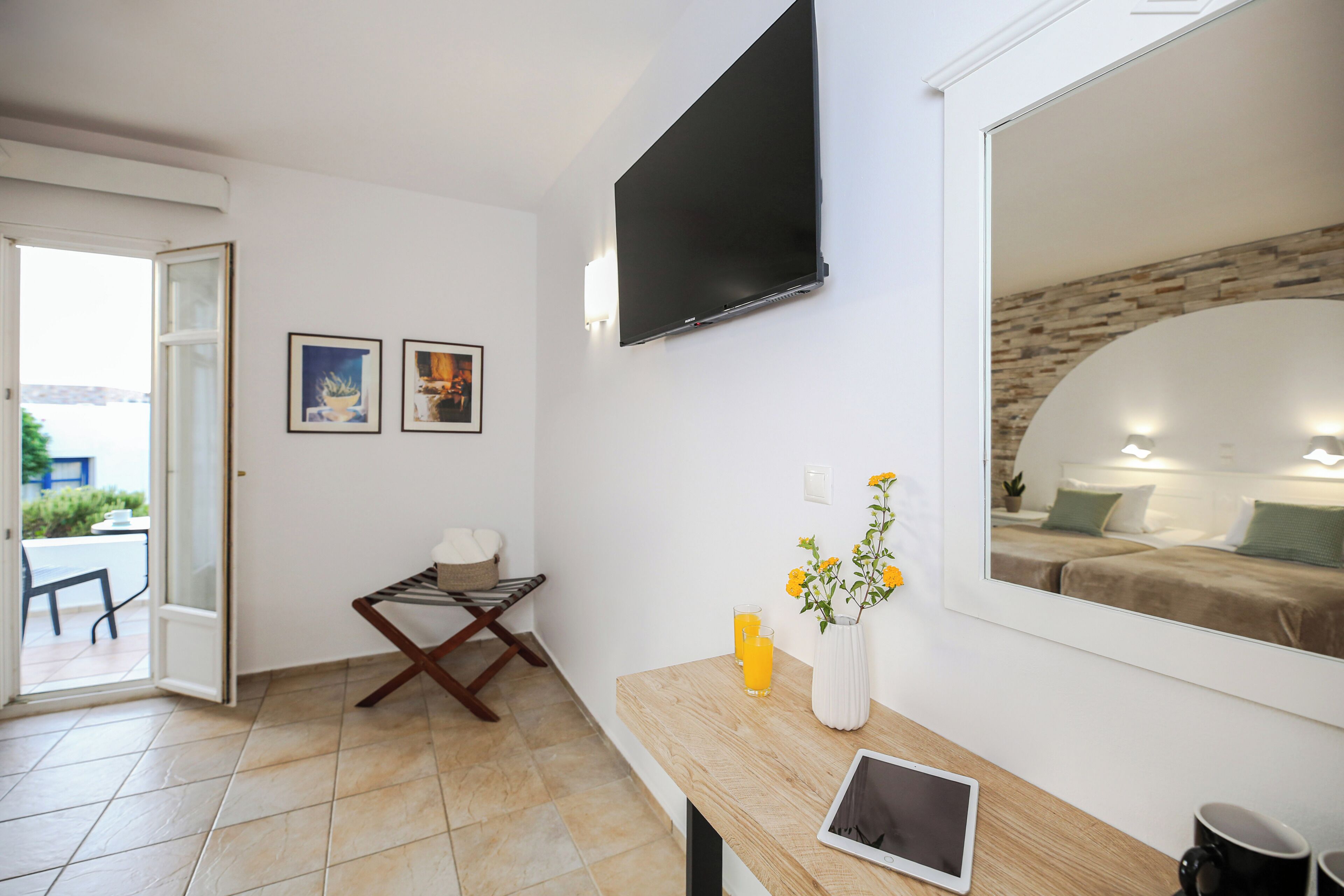 Une pièce comprenant un lit, un téléviseur, une table avec une tablette, un vase de fleurs et deux tableaux encadrés accrochés au mur.