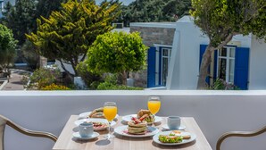A table set with breakfast items including croissants, pancakes, and fruit, with a view of a white building with blue shutters. - Naxos Palace Hotel (Naxos)