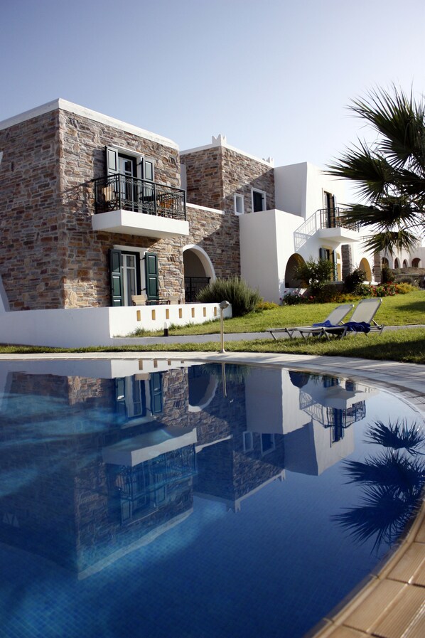 A modern building with stone facade, a pool, and two lounge chairs.