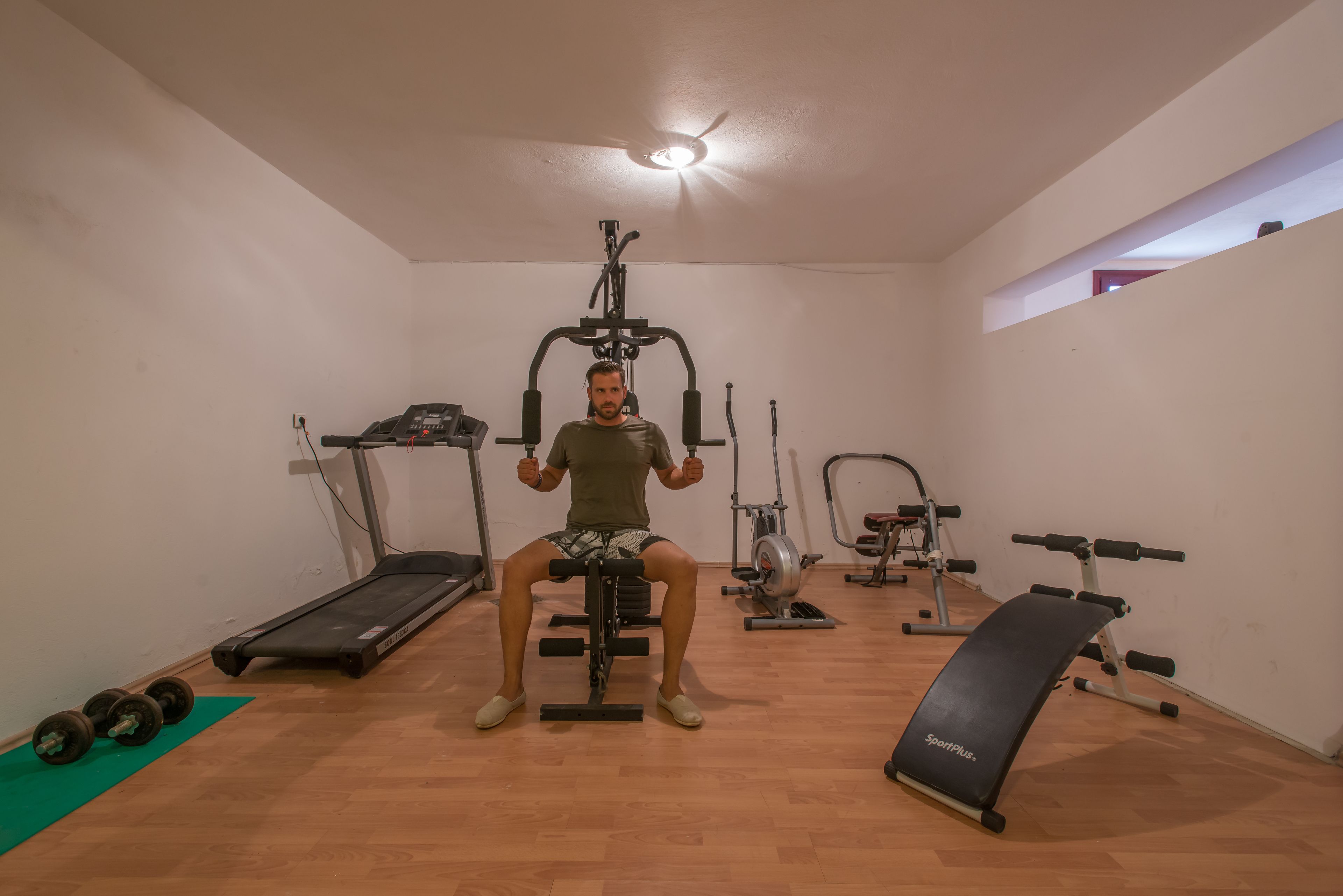 A home gym with a treadmill, weight bench, and exercise machine.