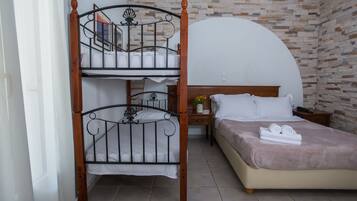 Una habitación con literas, una cama individual, una mesita de noche con lámpara y una pared con diseño de piedra.