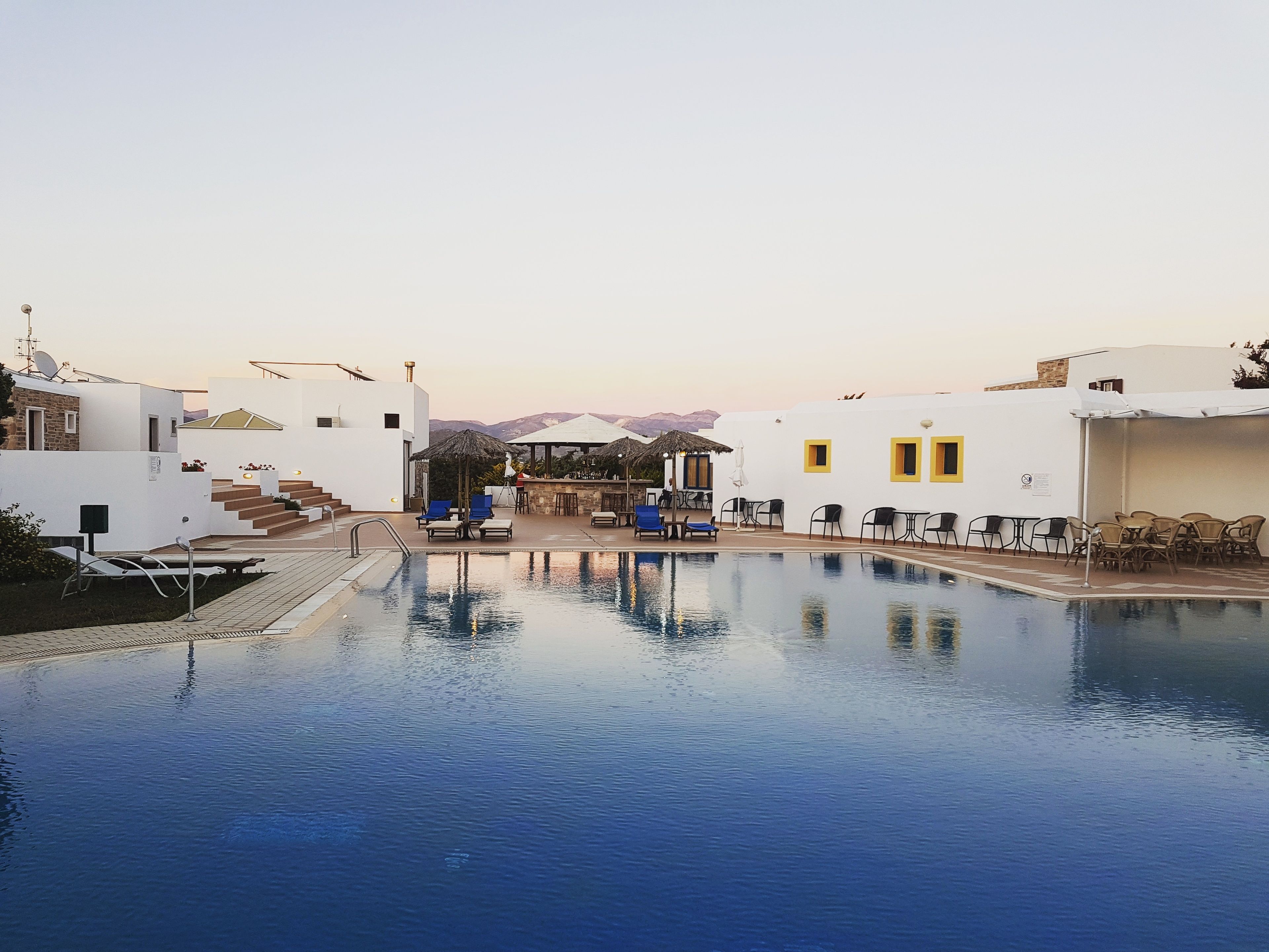 A pool area with lounge chairs and umbrellas, surrounded by white buildings with yellow accents.
