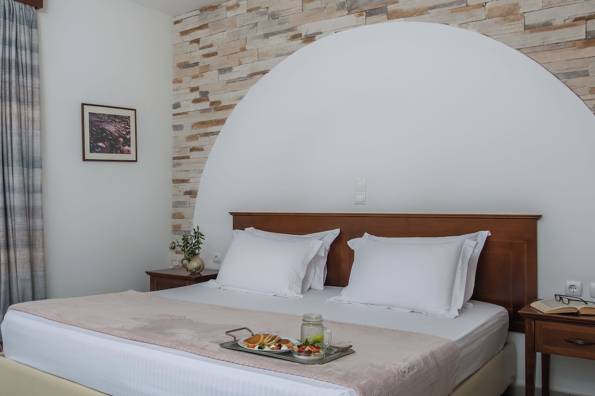 A neatly made bed with white linens, a tray of breakfast items, and a vase with a plant on the nightstand.