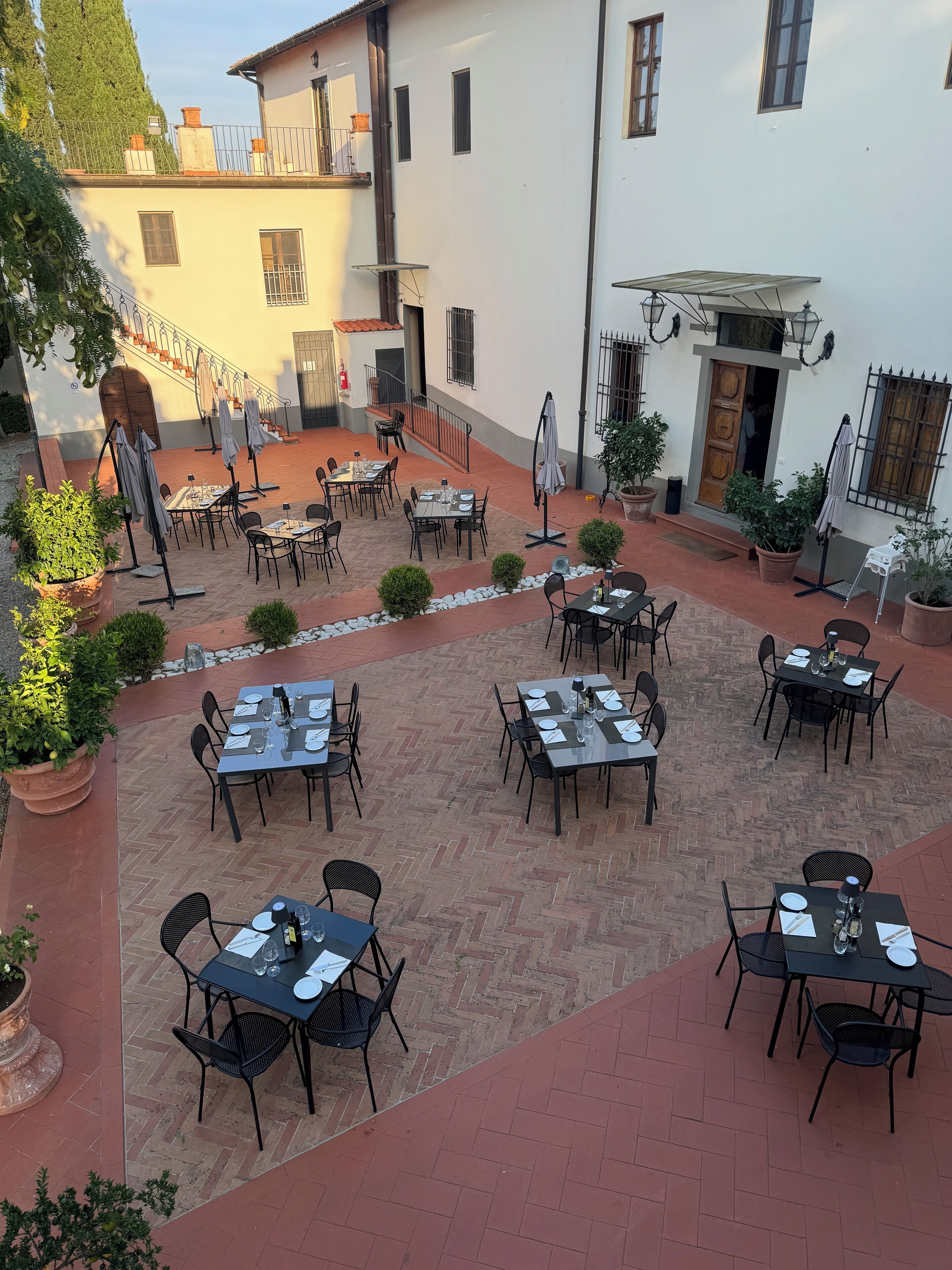 An outdoor patio with multiple tables and chairs, a staircase, and potted plants.