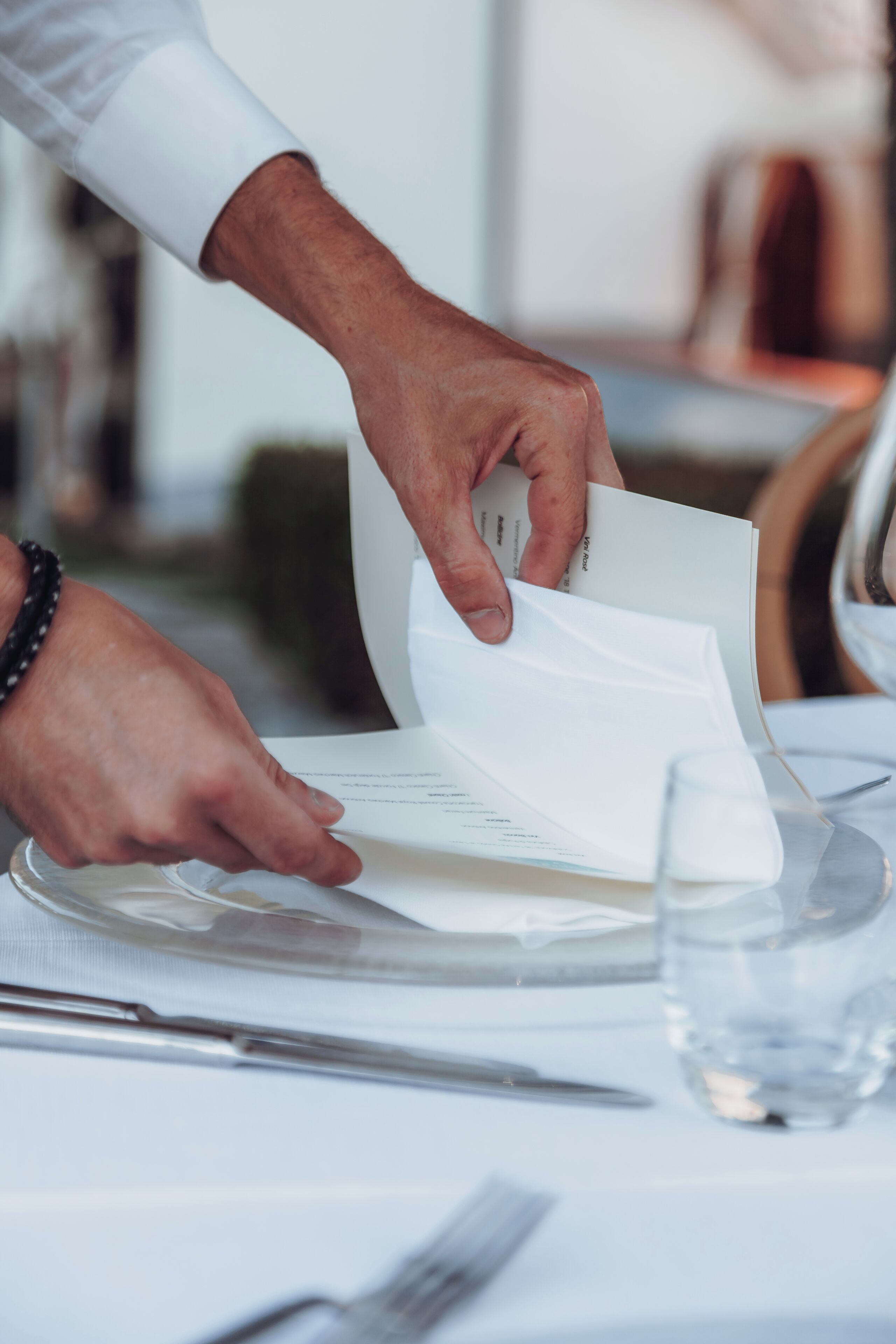 A person holding a menu at a table with a glass of water and a fork.