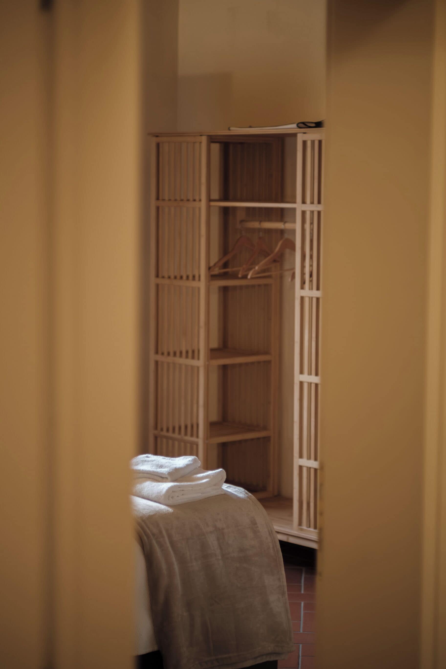 Un pasillo estrecho con un armario de madera y una cama con una manta blanca.