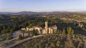 An aerial view of a church with a bell tower, surrounded by olive groves and a hilly landscape. - Villa Castiglione (Impruneta)