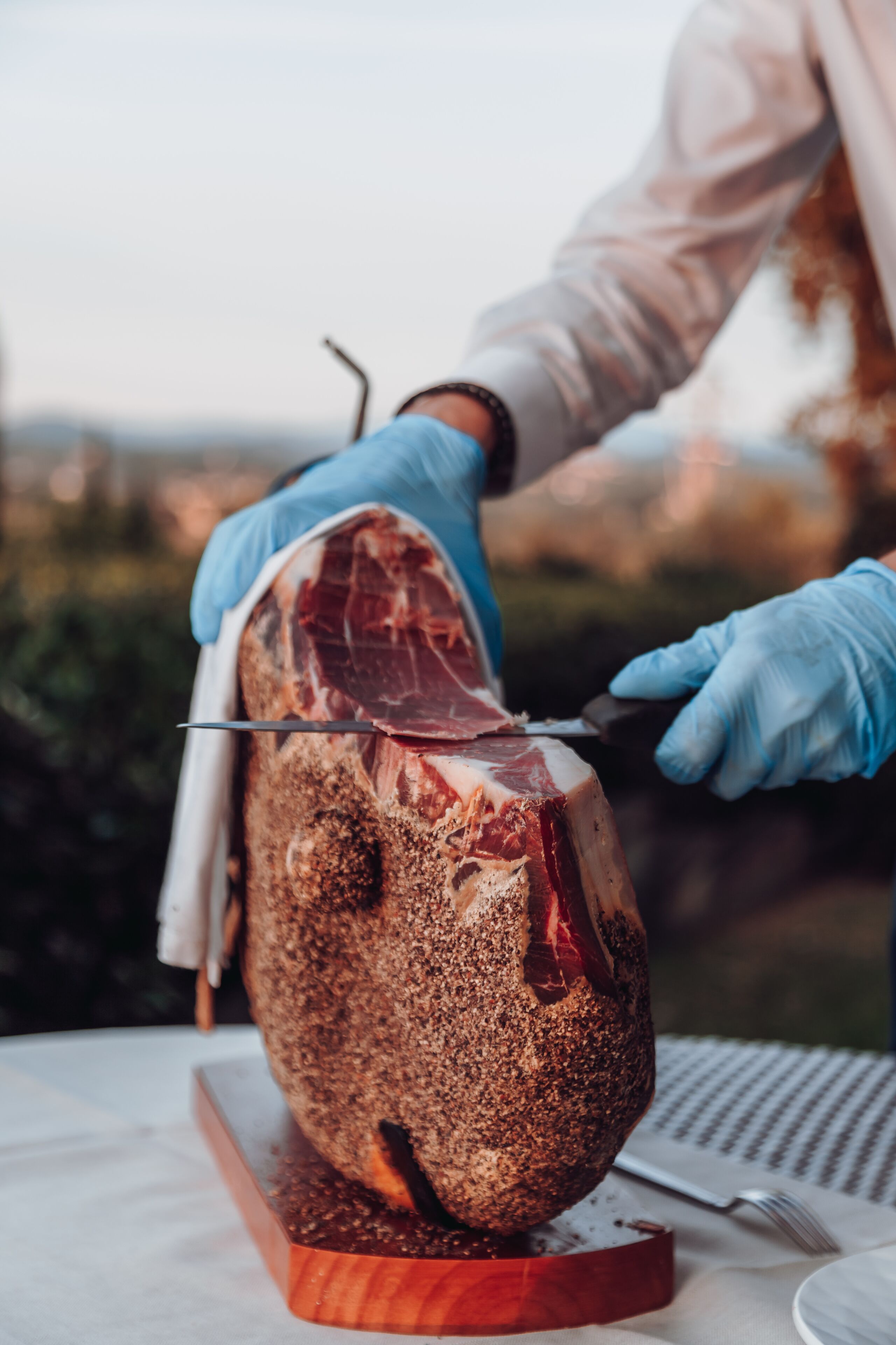Una persona con guantes cortando un trozo grande de carne sobre una tabla de madera.