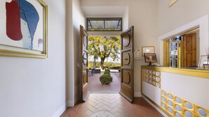 A hallway with a tiled floor, a reception desk with a gold and white color scheme, and a framed abstract painting on the wall. - Villa Castiglione (Impruneta)