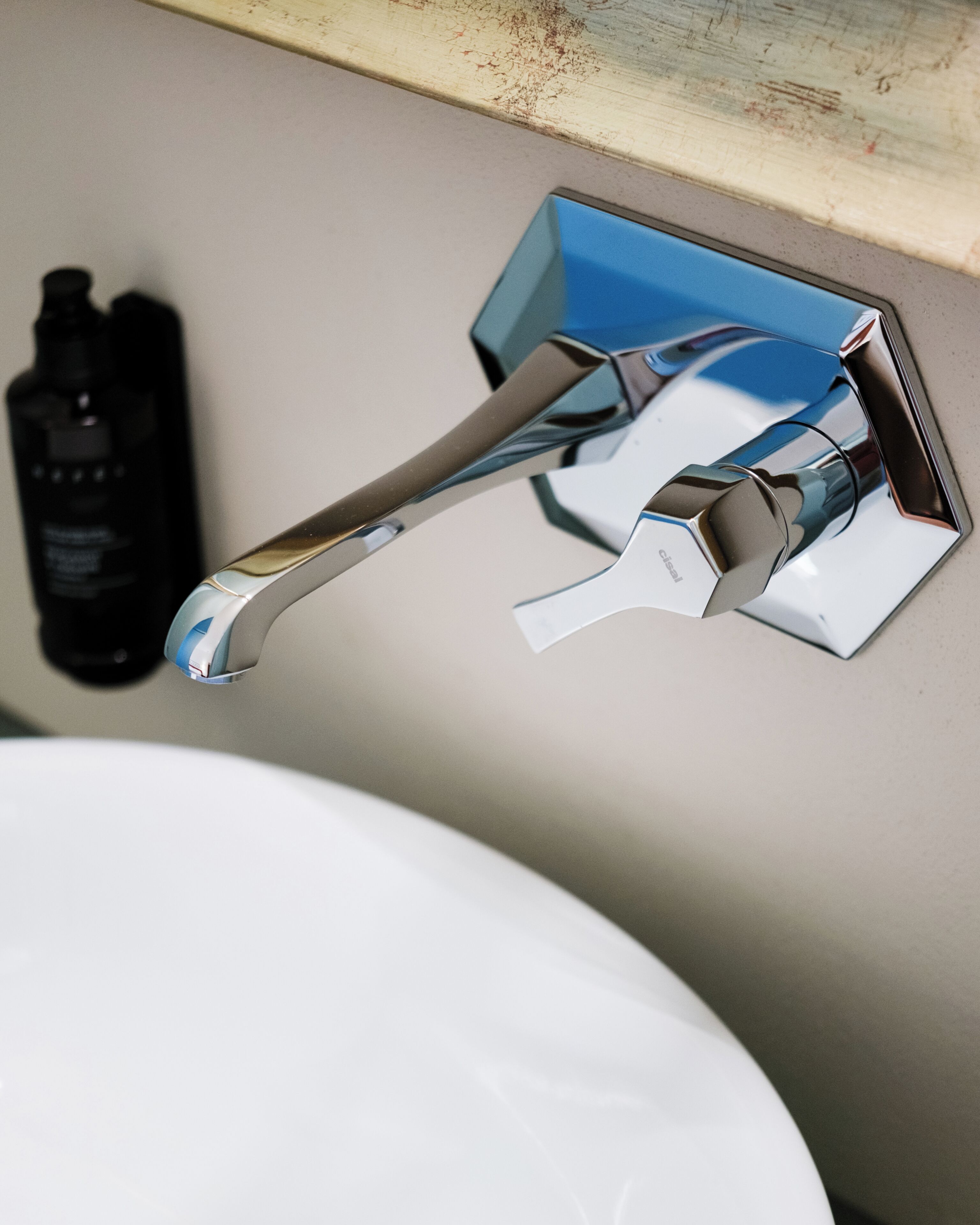 A chrome faucet mounted on a wall above a white sink.