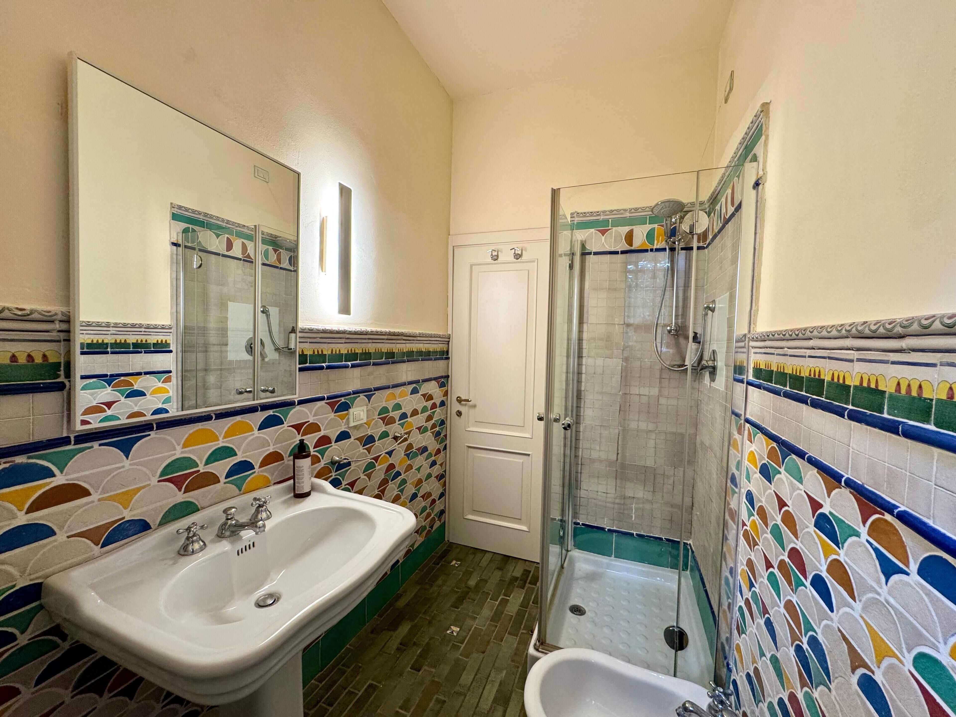 Un baño con lavamanos, espejo, ducha y paredes de azulejos.