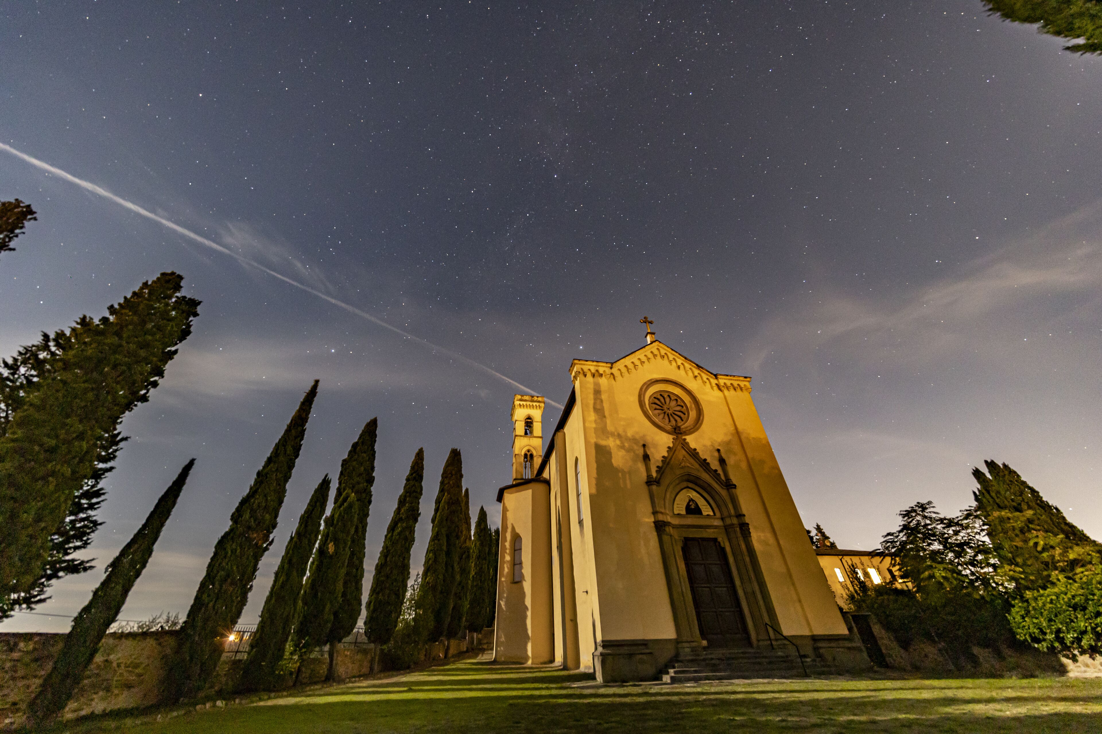 A church with a bell tower and a circular window, surrounded by tall cypress trees.
