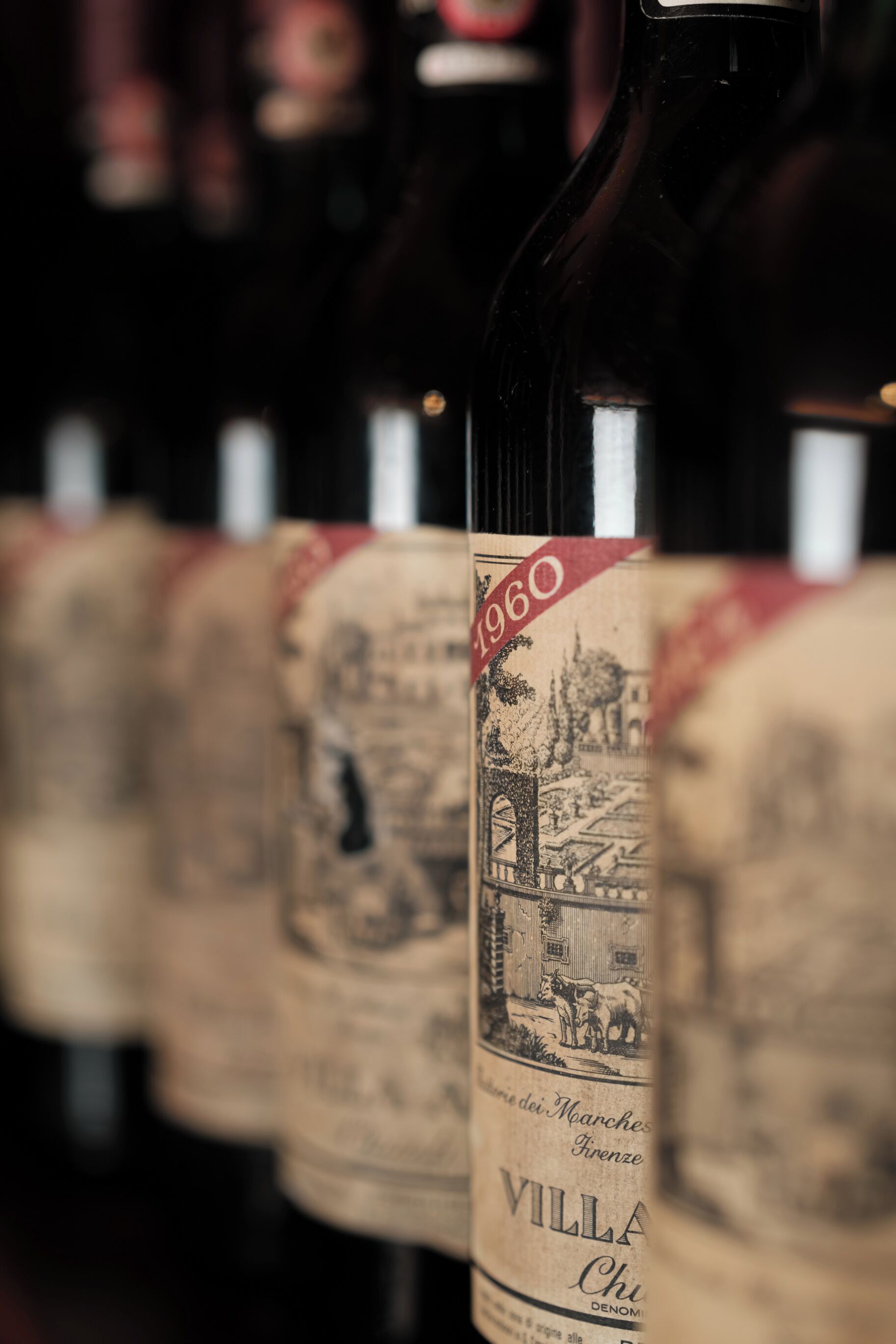 Una fila de botellas de vino con etiquetas, una de ellas muestra claramente '1960' y 'Villa Chu' de 'Firenze'.