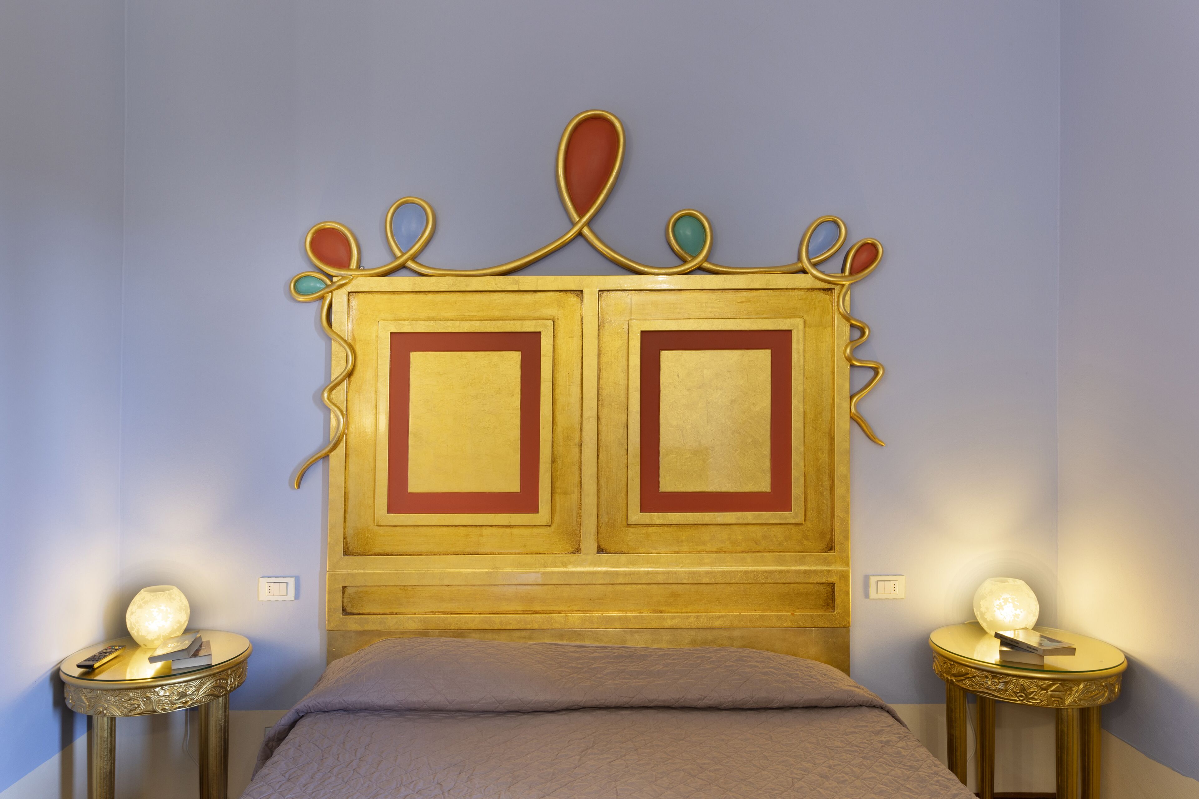 A bedroom with a double bed, two bedside tables with lamps, and a decorative headboard.