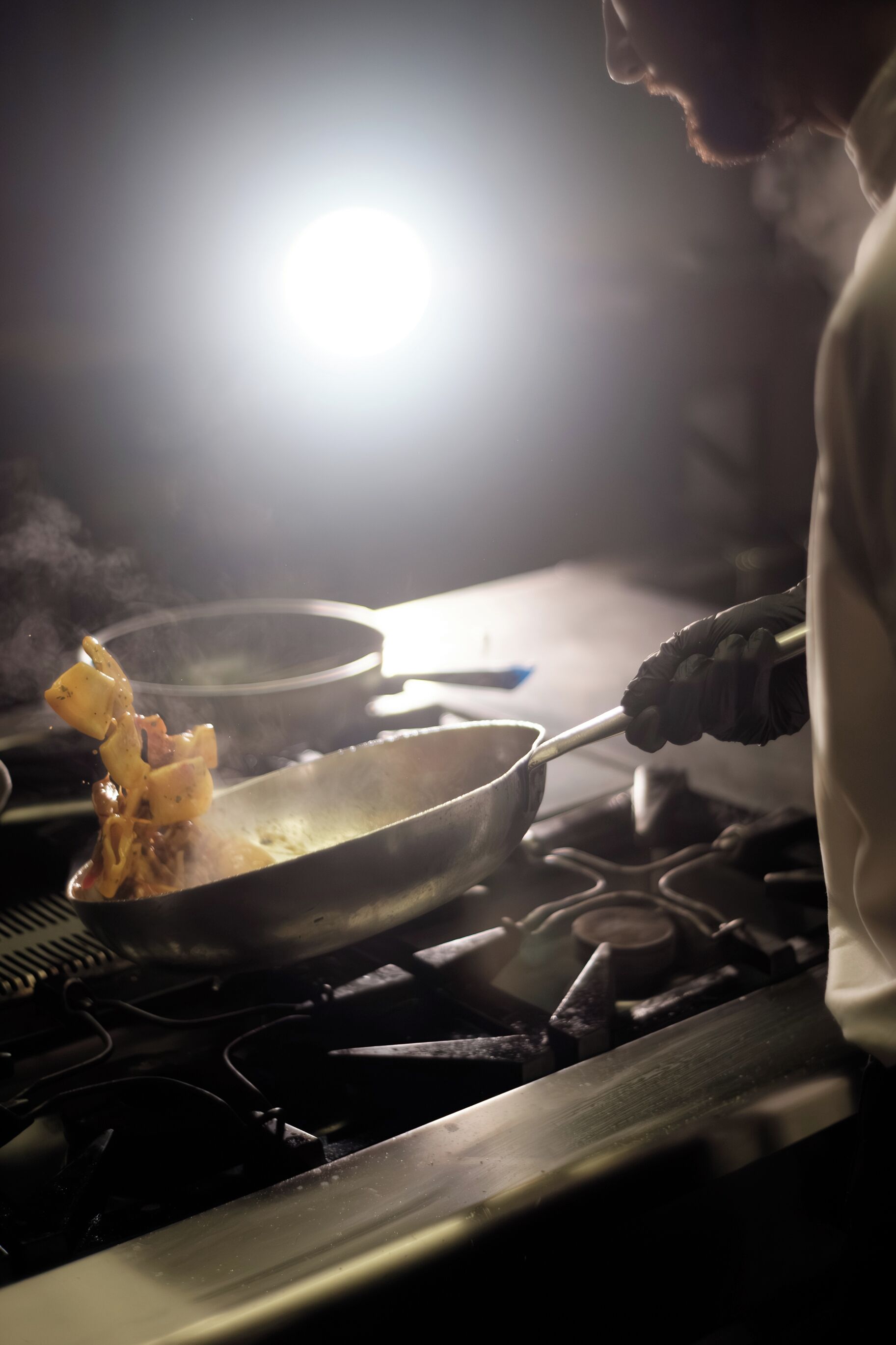 A person cooking with a pan on a stove, wearing gloves.