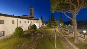 A courtyard with a building featuring a tower, surrounded by trees and potted plants. - Villa Castiglione (Impruneta)