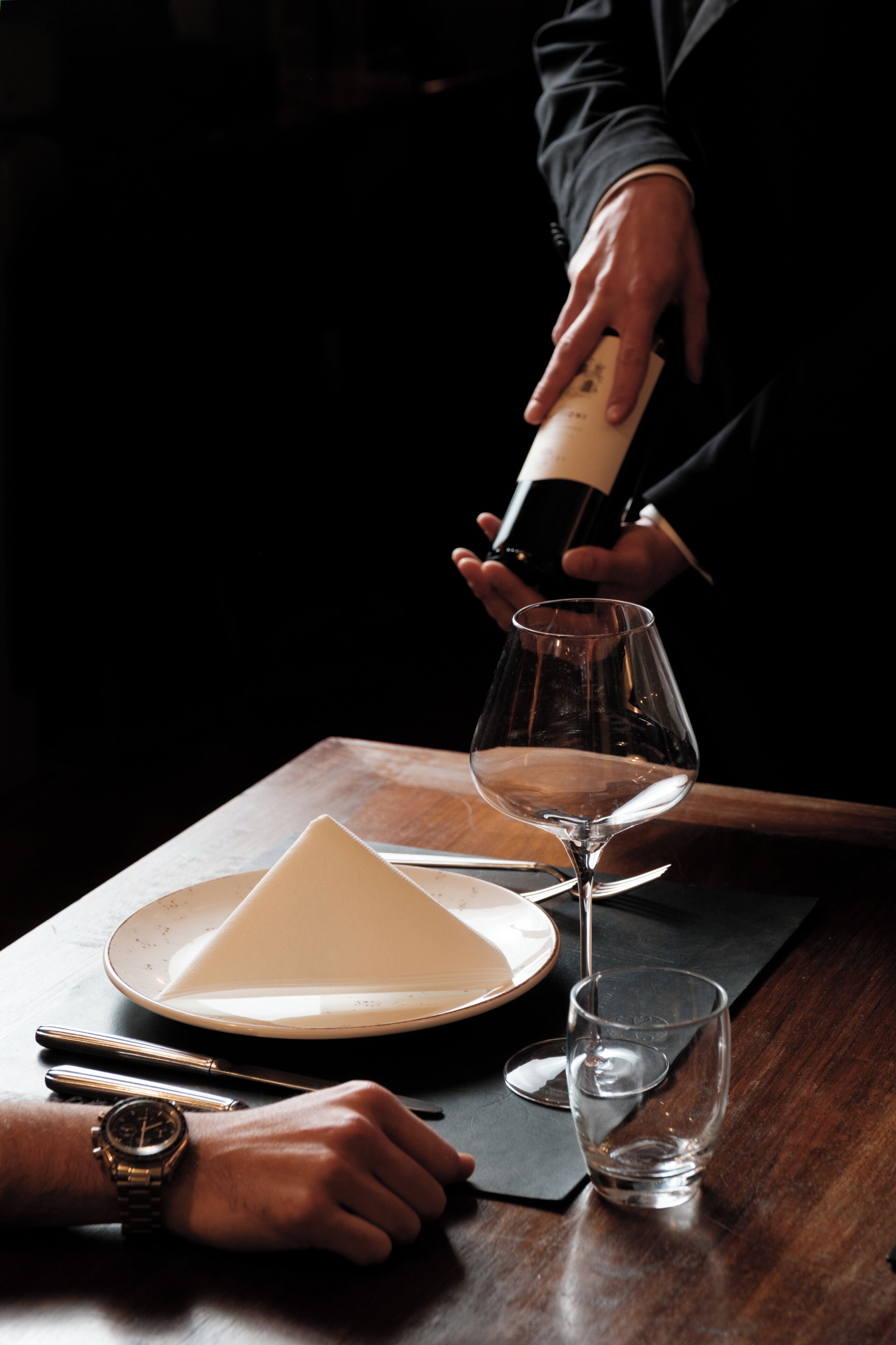 Iemand schenkt wijn in een glas, op een bord en een servetje op een tafel.