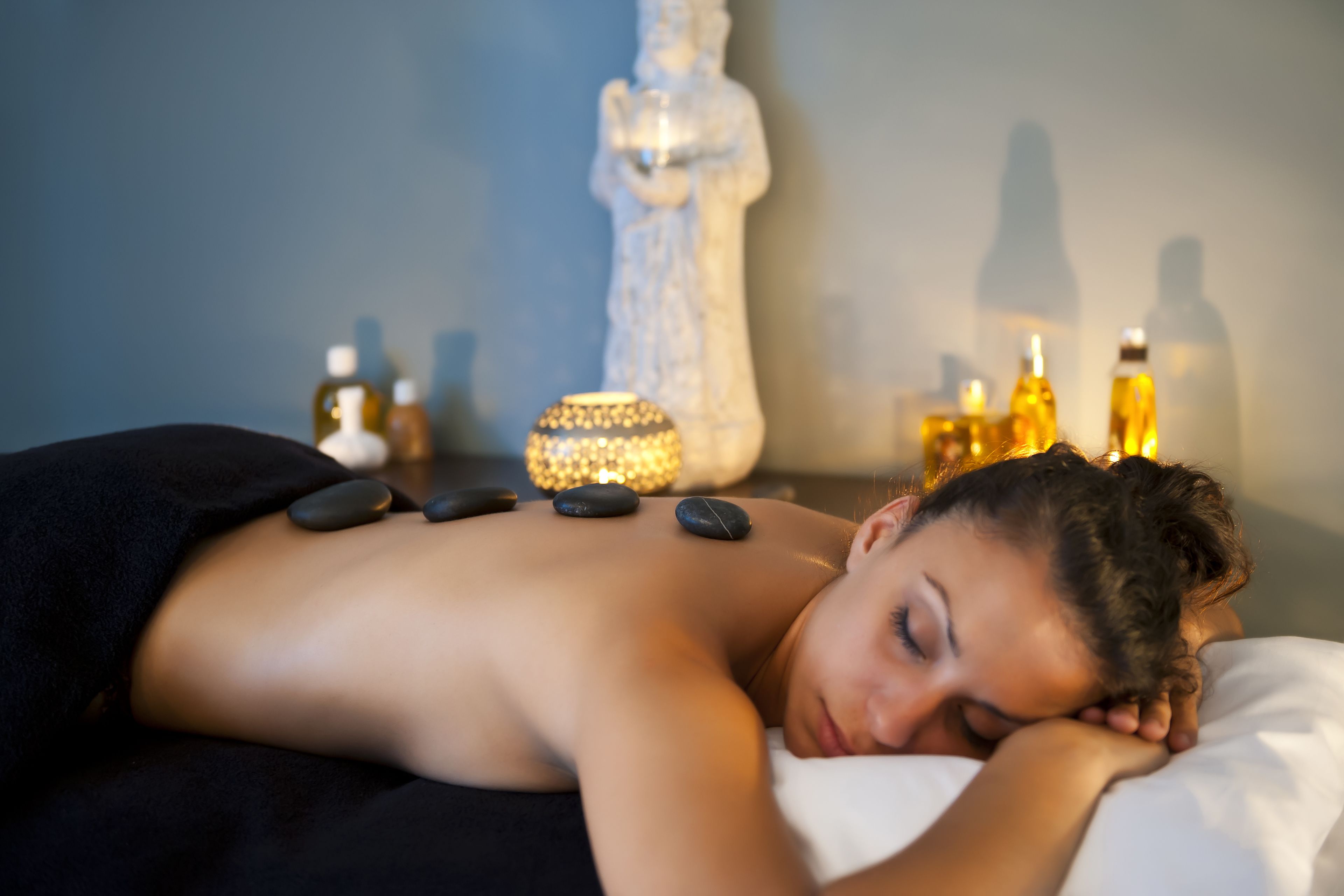 Une personne reçoit un massage du dos avec des pierres chaudes et des bougies dans un cadre de spa.