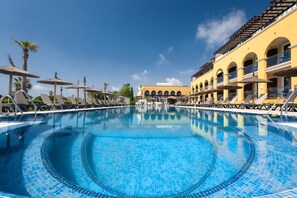 A large, clear blue pool with lounge chairs and umbrellas, surrounded by yellow buildings with arched windows and balconies. - Barceló Costa Ballena Golf & Spa (Rota)