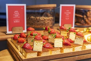 A dessert display with cheesecake squares topped with strawberries. - Barceló Costa Ballena Golf & Spa (Rota)