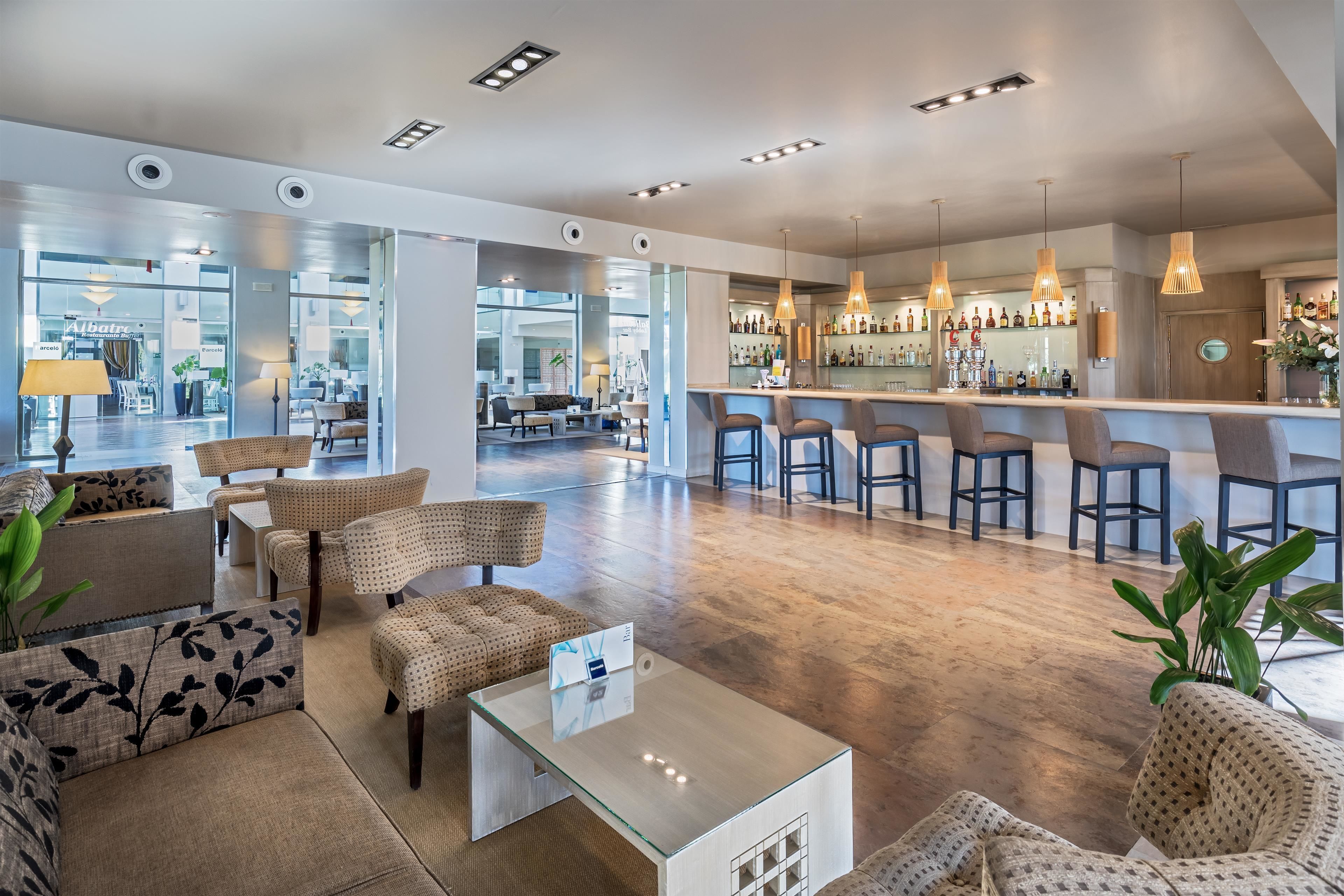 A modern hotel lobby with a bar area, seating arrangements, and a large window providing a view of the interior.