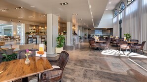 Un amplio vestíbulo de hotel con una barra central, zonas de estar y grandes ventanales que dejan entrar luz natural.