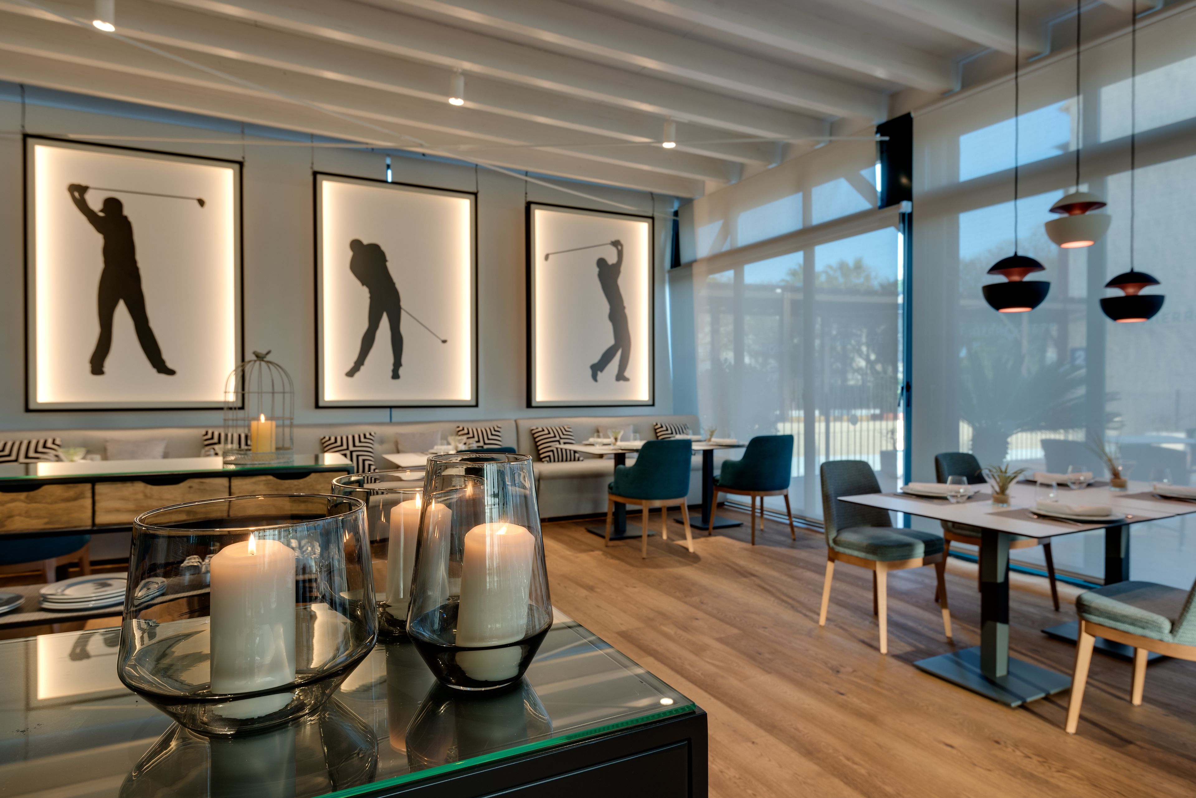 A modern dining area with a glass table, candles, and framed silhouettes of golfers.