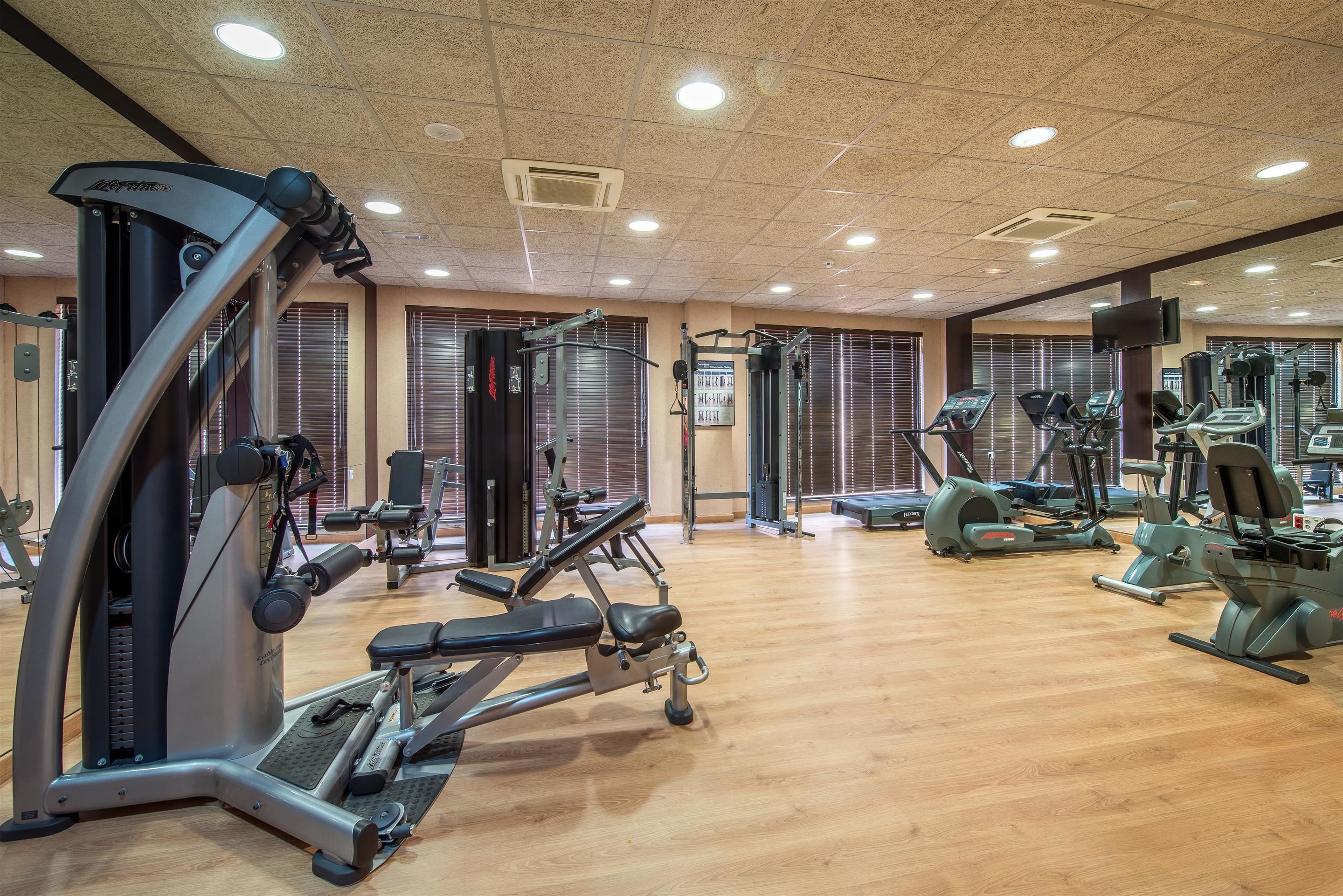 A gym with various exercise equipment, including treadmills and weight machines, and a wooden floor.