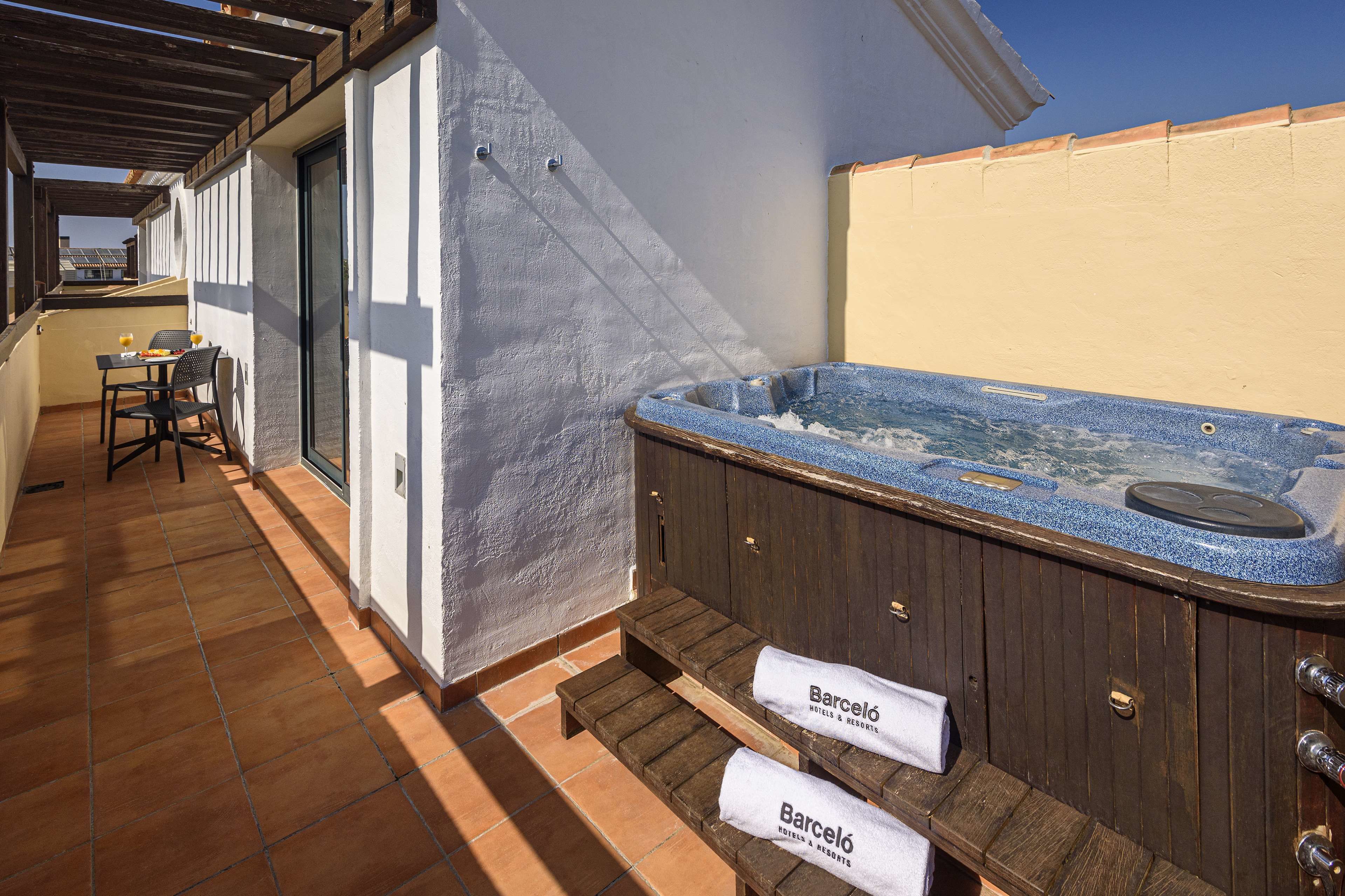 A spa area with a hot tub, wooden benches, and a table with chairs.