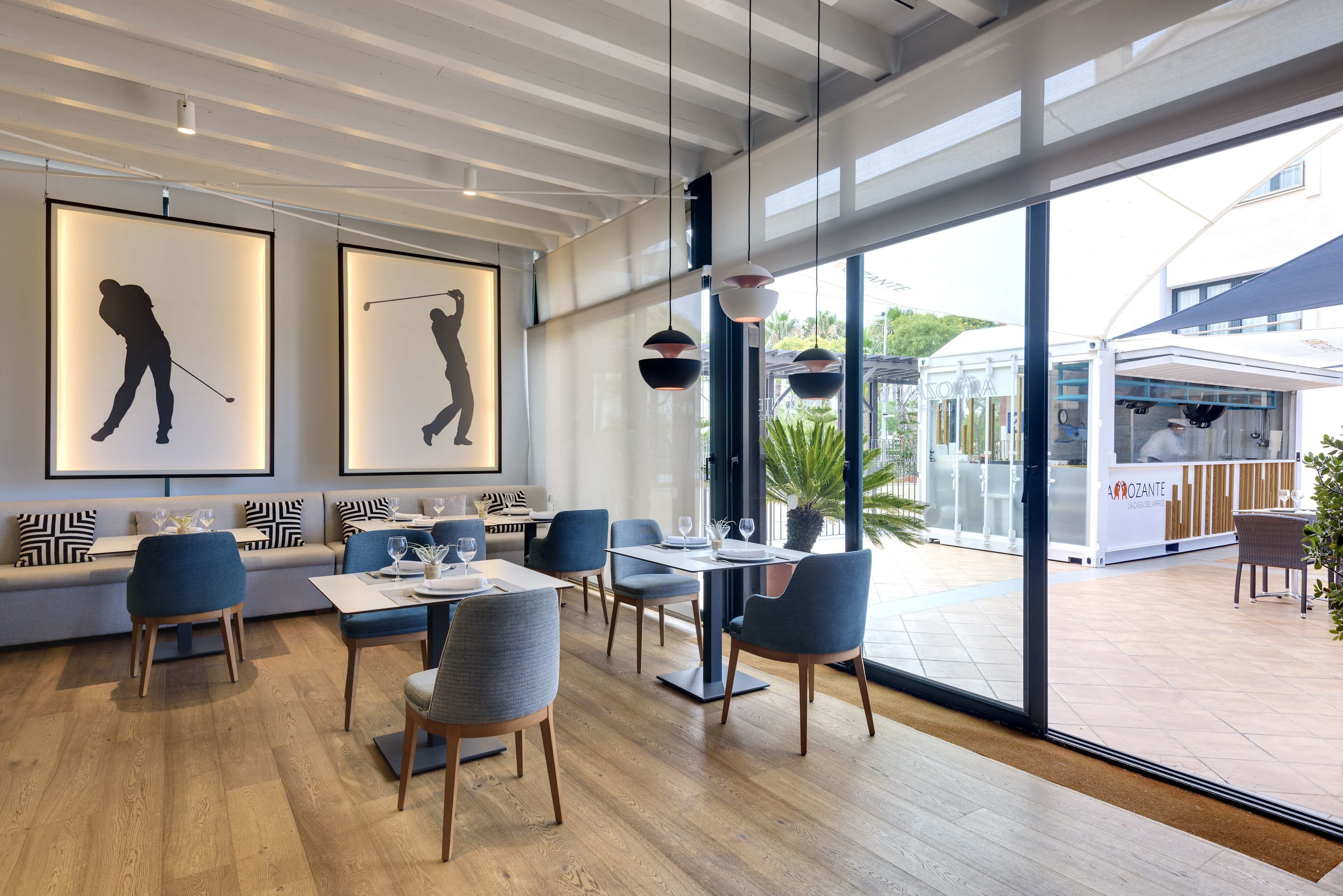 En moderne restaurant med trægulv, blå stole og borde. Væggene er dekoreret med indrammede silhuetter af golfspillere.