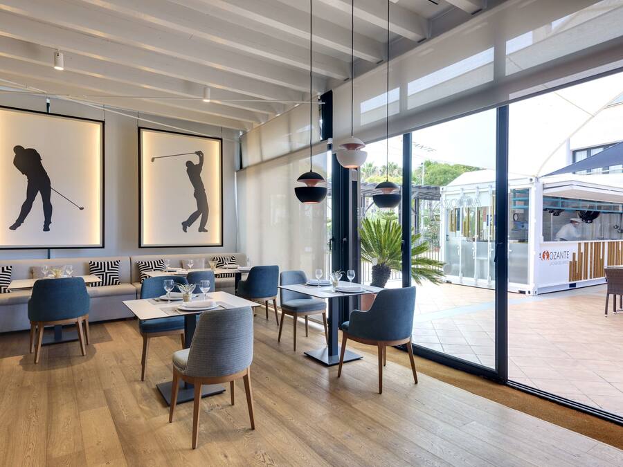 Un restaurante moderno con suelo de madera, sillas azules y mesas. En la pared, hay siluetas enmarcadas de golfistas.
