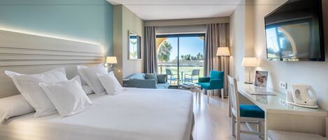Habitación de hotel con una cama grande, un escritorio con silla, un televisor y un balcón con vistas.