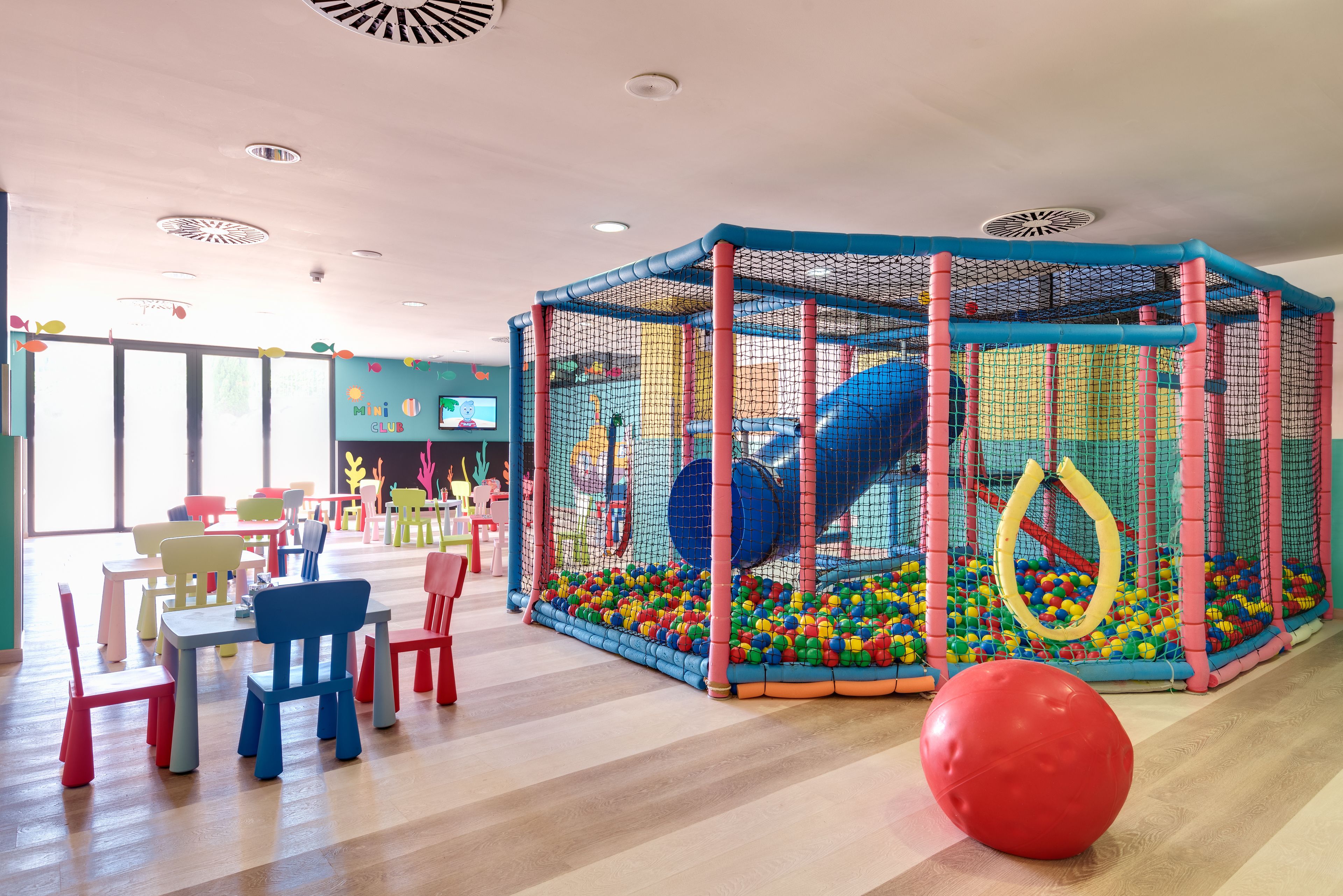 A play area with a ball pit and slides, surrounded by tables and chairs.